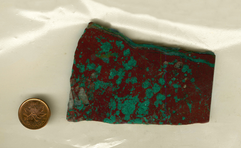 A slab of Cuprite and Malachite from Arizona, with bright green spots on a reddish brown surface, and one stripe of green stretching across the top.