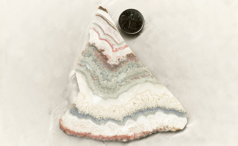 Pink and light blue stripes among white and cream-colored lace patterns in a slab of Cactus Lace Agate rom Mexico.
