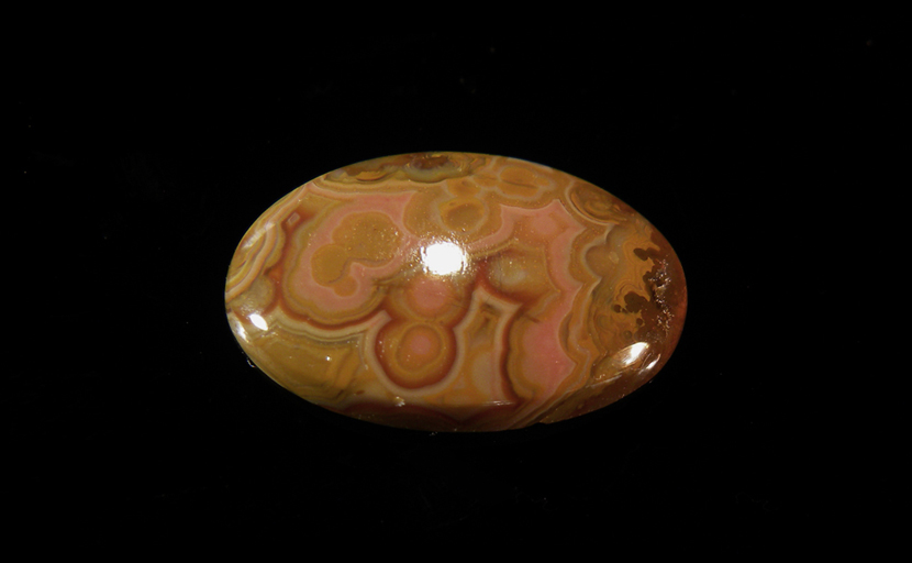 Calibrated oval polished Fairburn Agate cabochon from Nebraska or South Dakota, with green spheres in a pink, brown and gray patterned background.