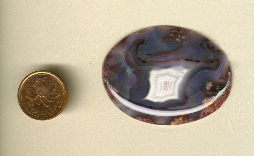 Calibrated oval polished Parcelas Agate cabochon from Mexico, with purple, blue and red patterns built around a central white fortification.