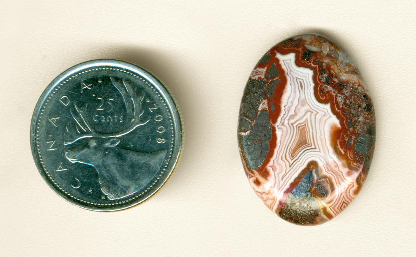 Polished Crazy Lace Agate cabochon, with an "A"-shaped pink fortification and red and metallic moss inclusions.