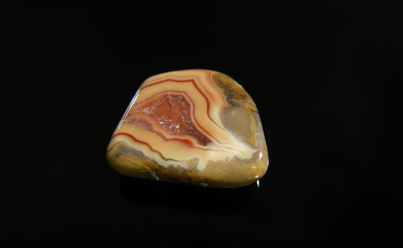 A freeform Fairburn Agate from Nebraska or South Dakota, with concentric red patterns on a light orange background, with a central cavity that shows rough quartz crystals.