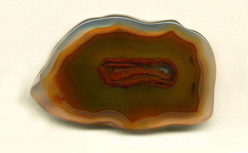 A freeform Coyamito Agate from Mexico, brown and clear, with a brighter red central membrane shape.