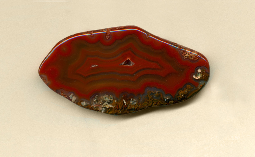 A freeform Coyamito Agate from Mexico with bright, strong red fortifications resting on a blanket of green moss patterns.