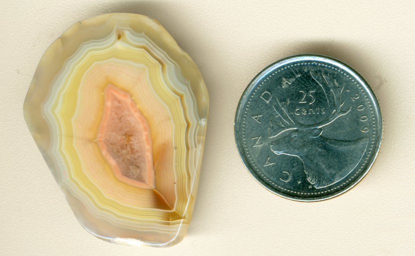 Pink, white and yellow bands around a vug of crystals in a freeform polished Moctezuma Agate from Mexico.