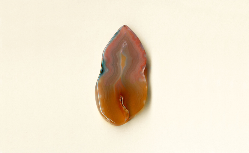 A freeform Coyamito Agate from Mexico, shaped like a candle flame, with orange toward the bottom, fading to pink toward the top, highlighted by blue.