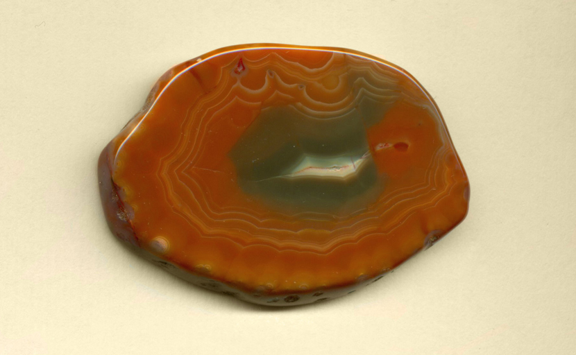 A freeform polished Coyamito Agate from Mexico, with an orange mantle all around a green center and faint white fortifications overlaying it.