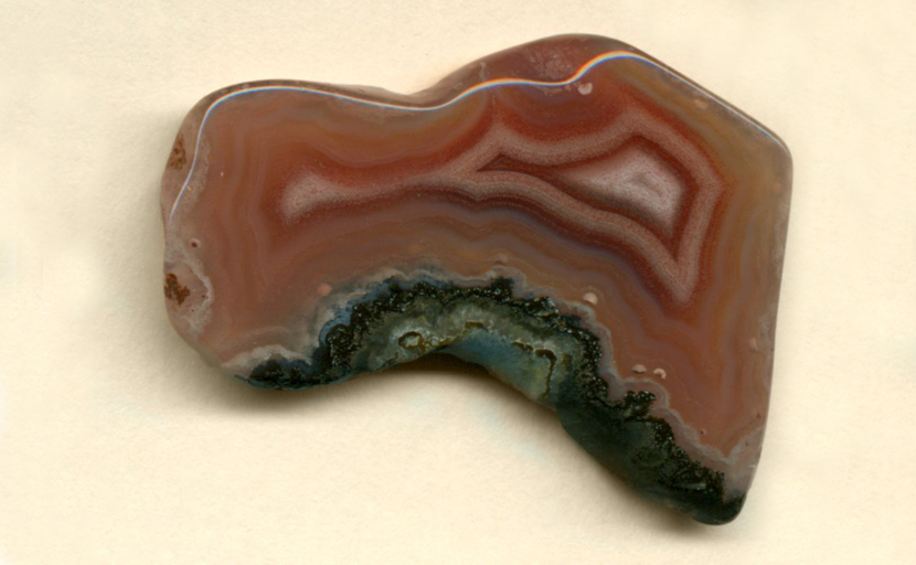 A polished, strangely shaped freeform Coyamito Agate from Mexico, orange and red with an elongated white fortification pattern in the center.