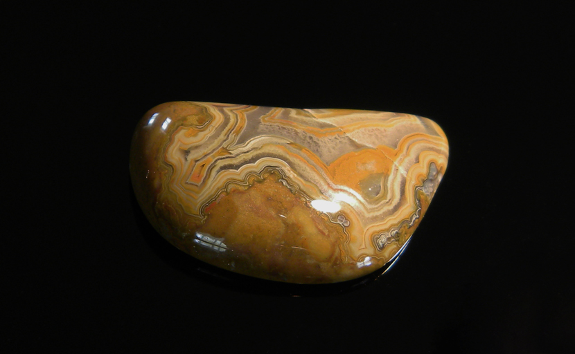 A freeform cabochon of Fairburn Agate from Nebraska or South Dakota, orange and brown in a fortification pattern, lacy around the edges.