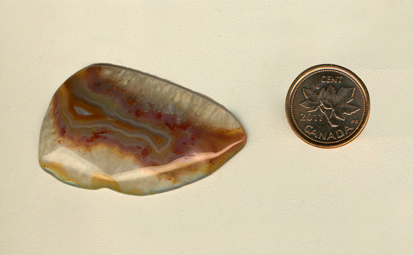 Freeform polished Coyamito Agate cabochon from Mexico, clear with a central yellow and orange fortification, which is covered in red and purple flames.