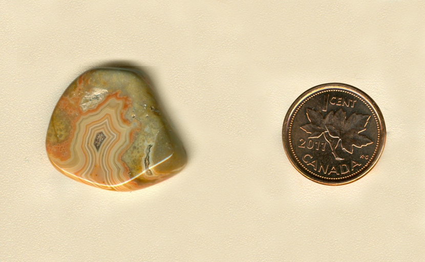 Freeform polished Fairburn Agate from Nebraska or South Dakota, with a central orange and yellow pattern on a green background, with bubbles around its edge.