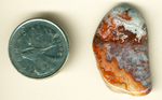 White fortifications and orange lace on either side of a blue and red space, arranged like a miniature map, in a polished freeform Crazy Lace Agate from Mexico.